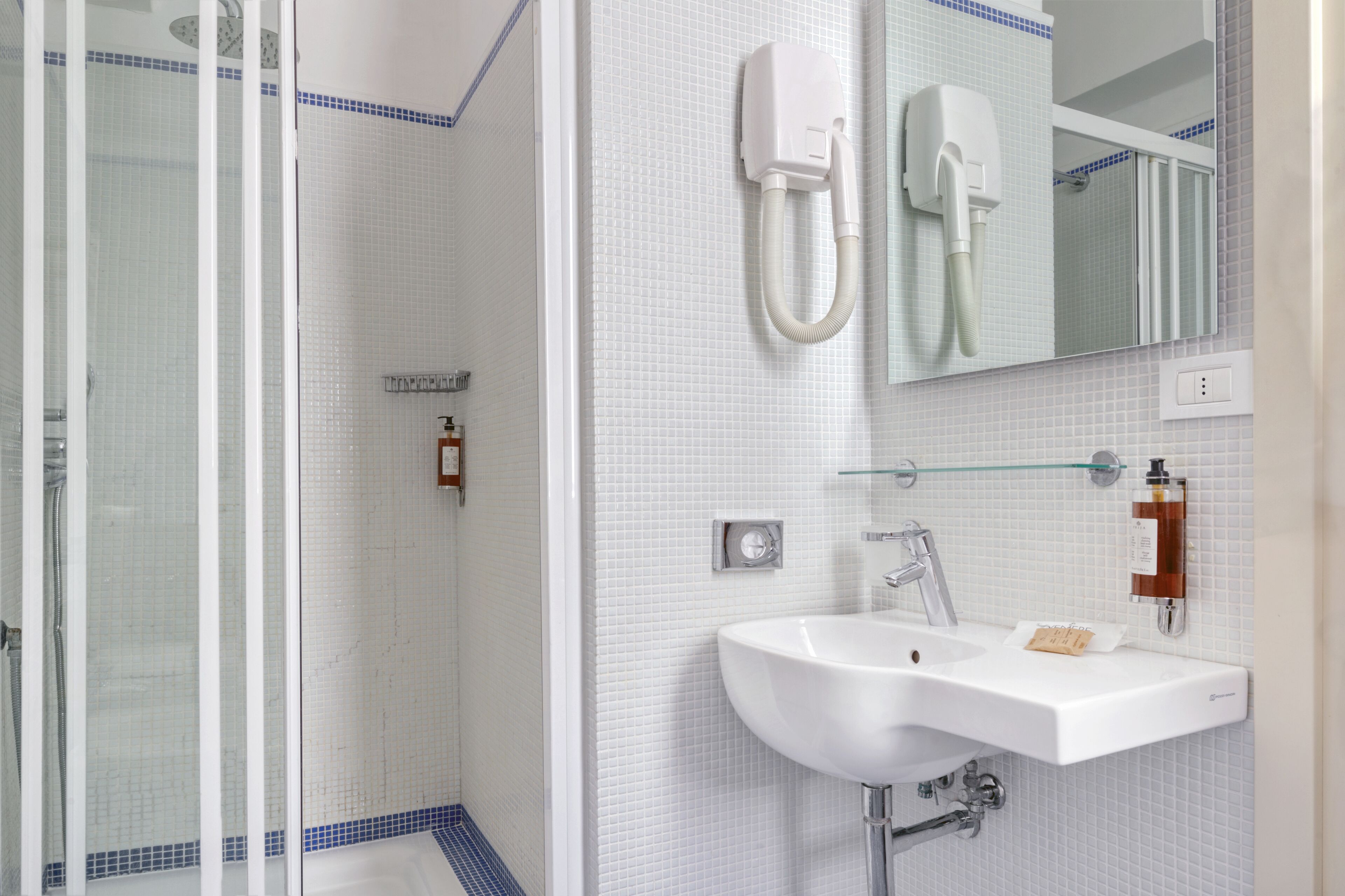 Ein Badezimmer mit Duschkabine aus Glas, einem weißen Waschbecken mit Spiegel darüber und einem an der Wand befestigten Händetrockner.