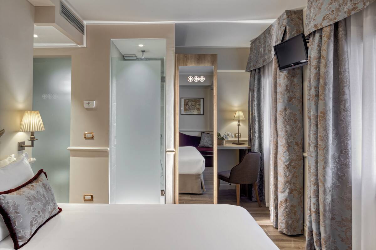Ein Hotelzimmer mit Bett, Schreibtisch, Stuhl und einem an der Wand befestigten Fernseher.