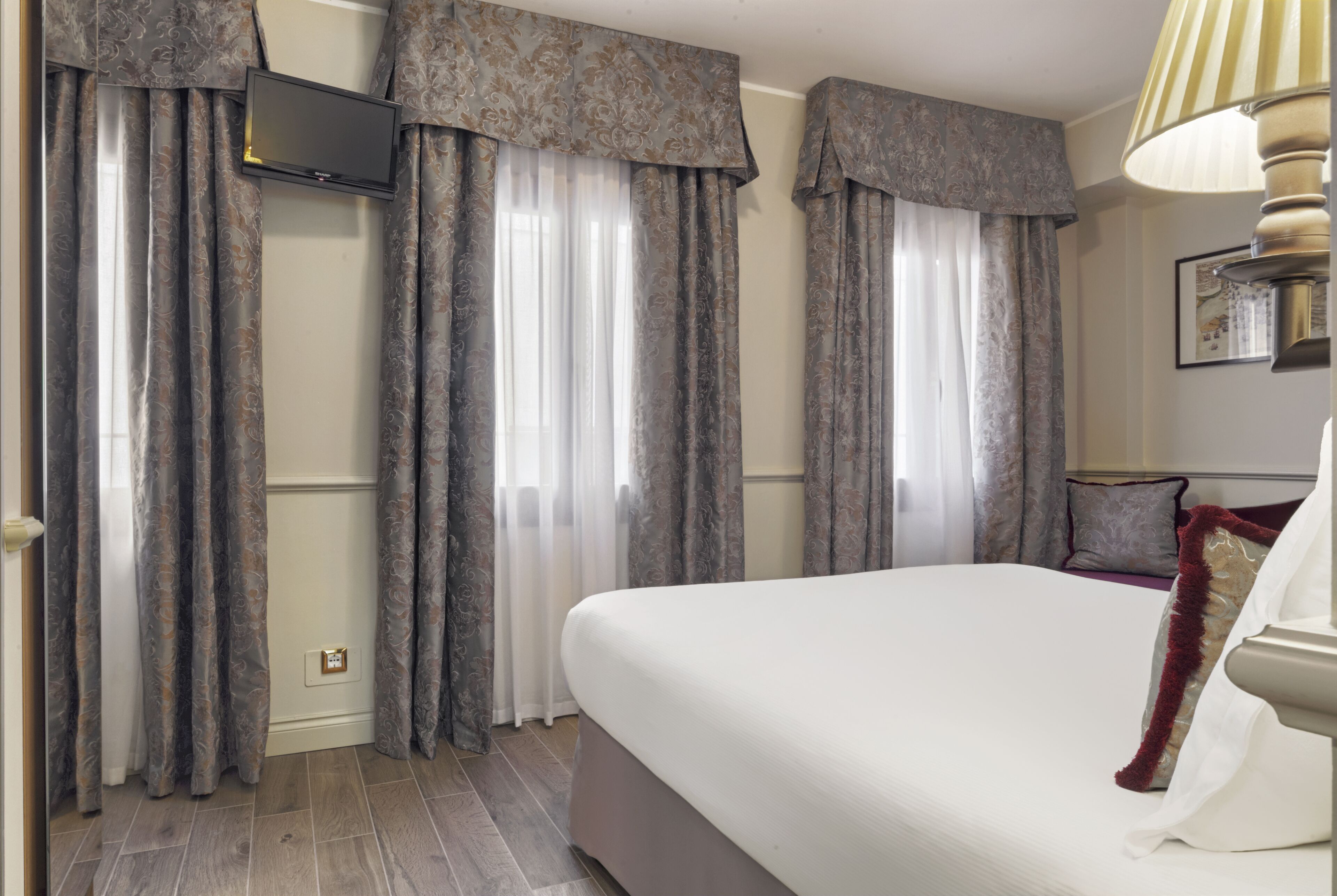 A hotel room with a large bed, a flat-screen TV mounted on the wall, and a lamp on the nightstand.
