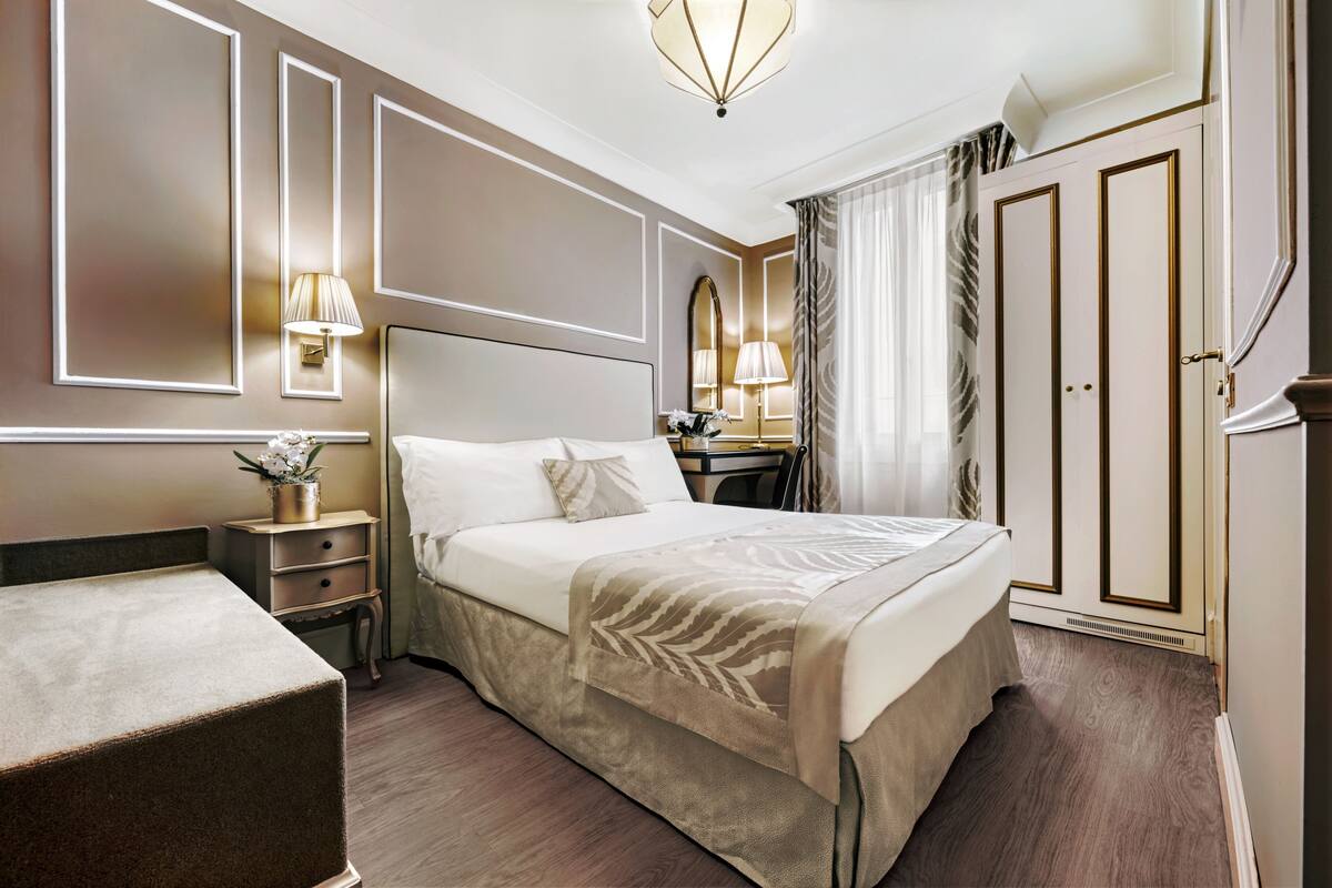 Ein Hotelzimmer mit einem großen Bett, Nachttischen, einem Schreibtisch und einem Kleiderschrank.