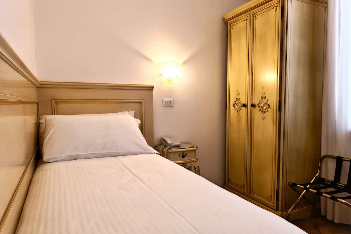 Un letto rifatto con cura, un comodino con il telefono e un armadio con maniglie decorative.