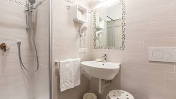 A modern bathroom with a glass-enclosed shower, a white sink, and a small stool.