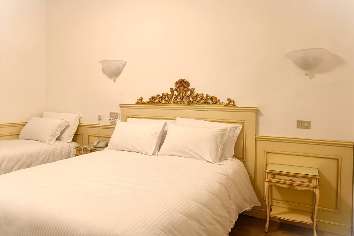 Camera d'albergo con due letti, una testiera decorativa, comodini e lampade a parete.