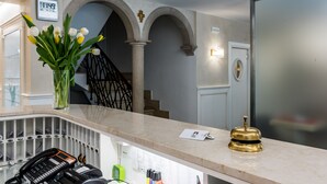 A hotel reception area with a marble counter, a telephone, a vase with flowers, and a bell. - Hotel Guerrini (Venice)