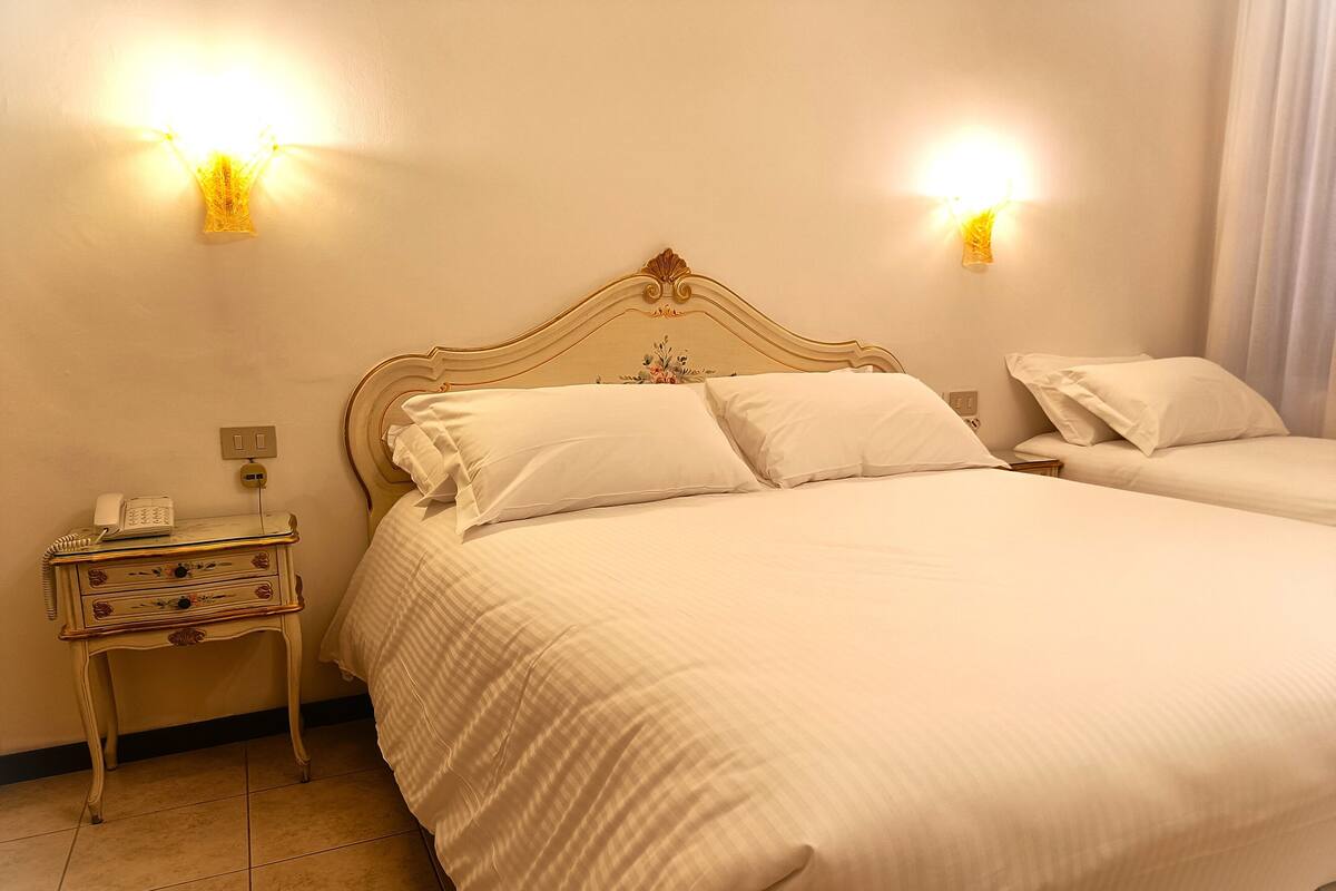 Una camera d'albergo con un letto grande, un comodino con un telefono e due luci fissate al muro.