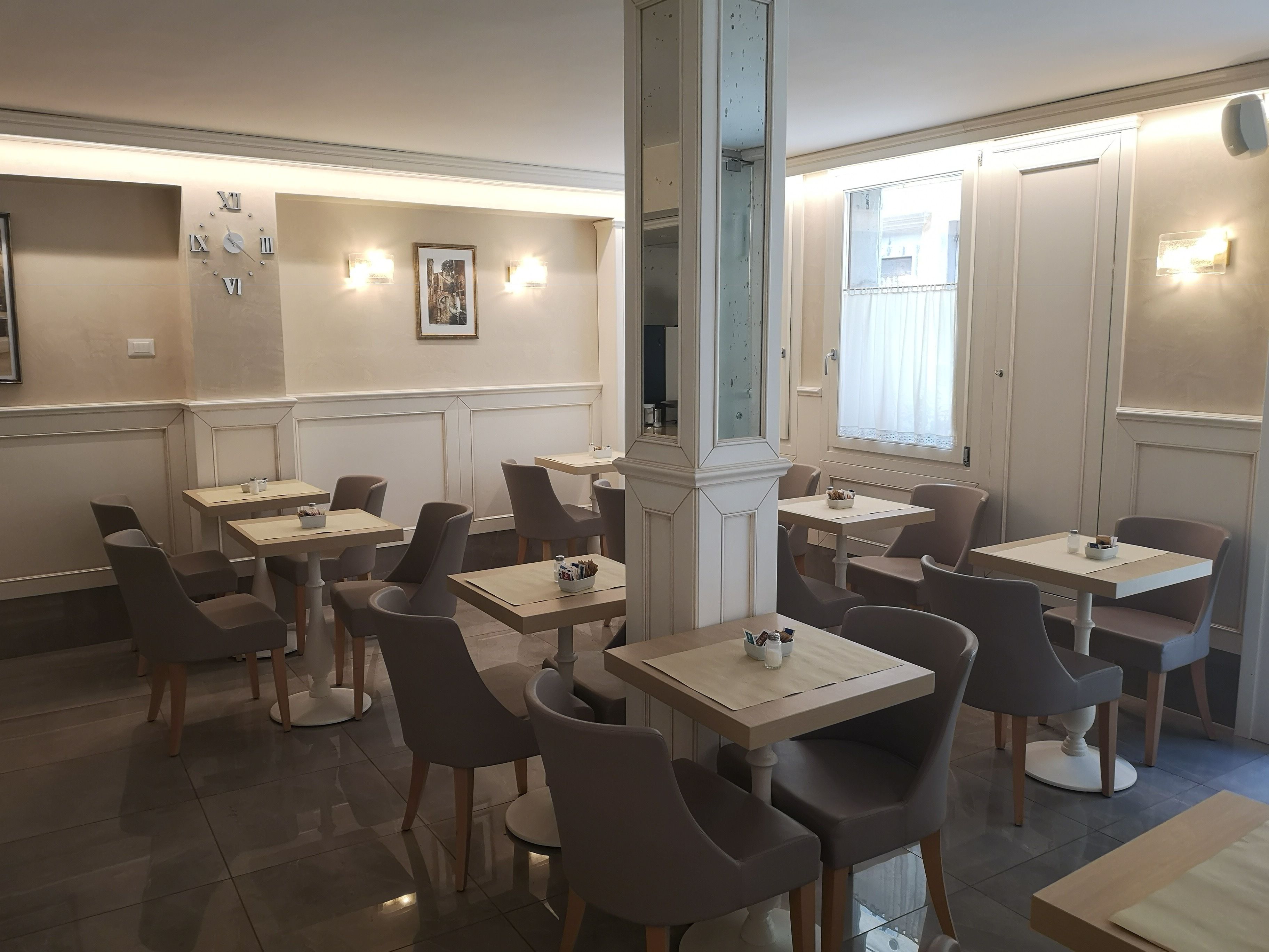 Un interior de restaurante moderno con varias mesas y sillas, un gran reloj de pared y obras de arte enmarcadas.