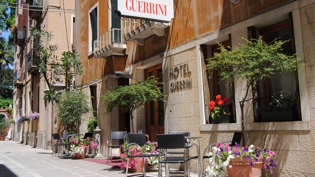 A hotel named "Hotel Guerrini" with outdoor seating, potted plants, and a clear view of the street. - Hotel Guerrini (Venice)