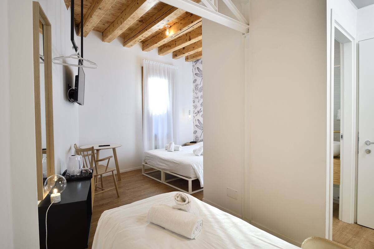 A bedroom with a bed, a desk with a lamp, a chair, and a wardrobe.