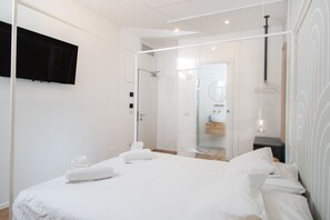A modern bedroom with a large bed, a glass shower enclosure, and a mounted TV. - Rio Hotel (Venice)