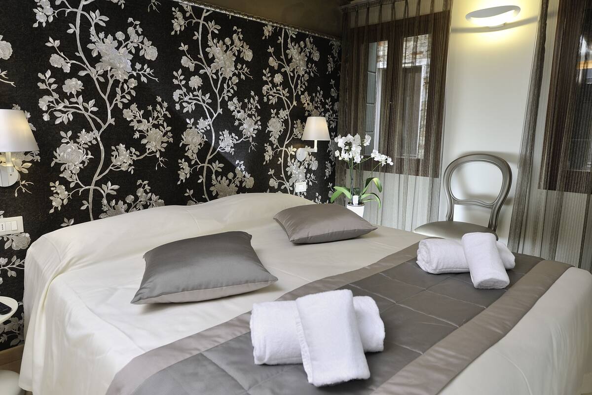 A neatly made bed with white and gray linens, a bedside lamp, and a potted orchid on the nightstand.
