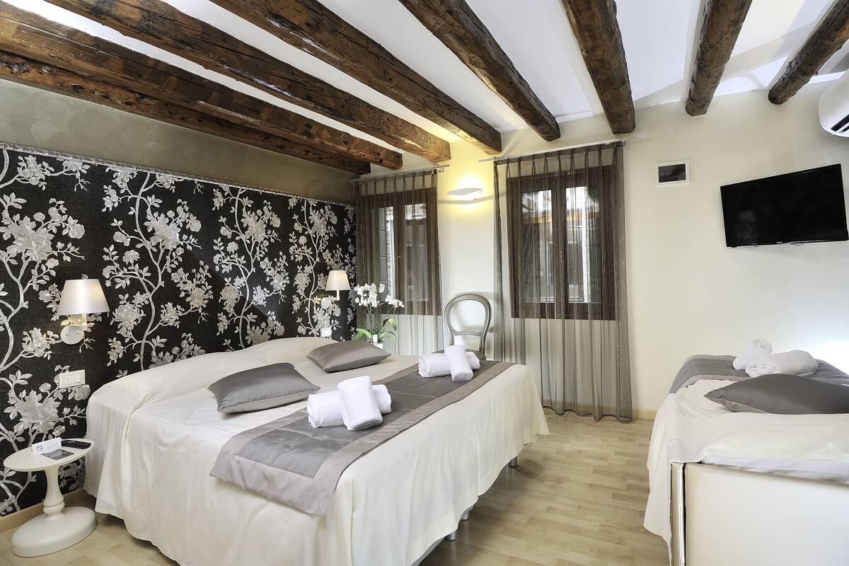 A hotel room with two beds, a TV, a mirror, and a floral wallpaper.