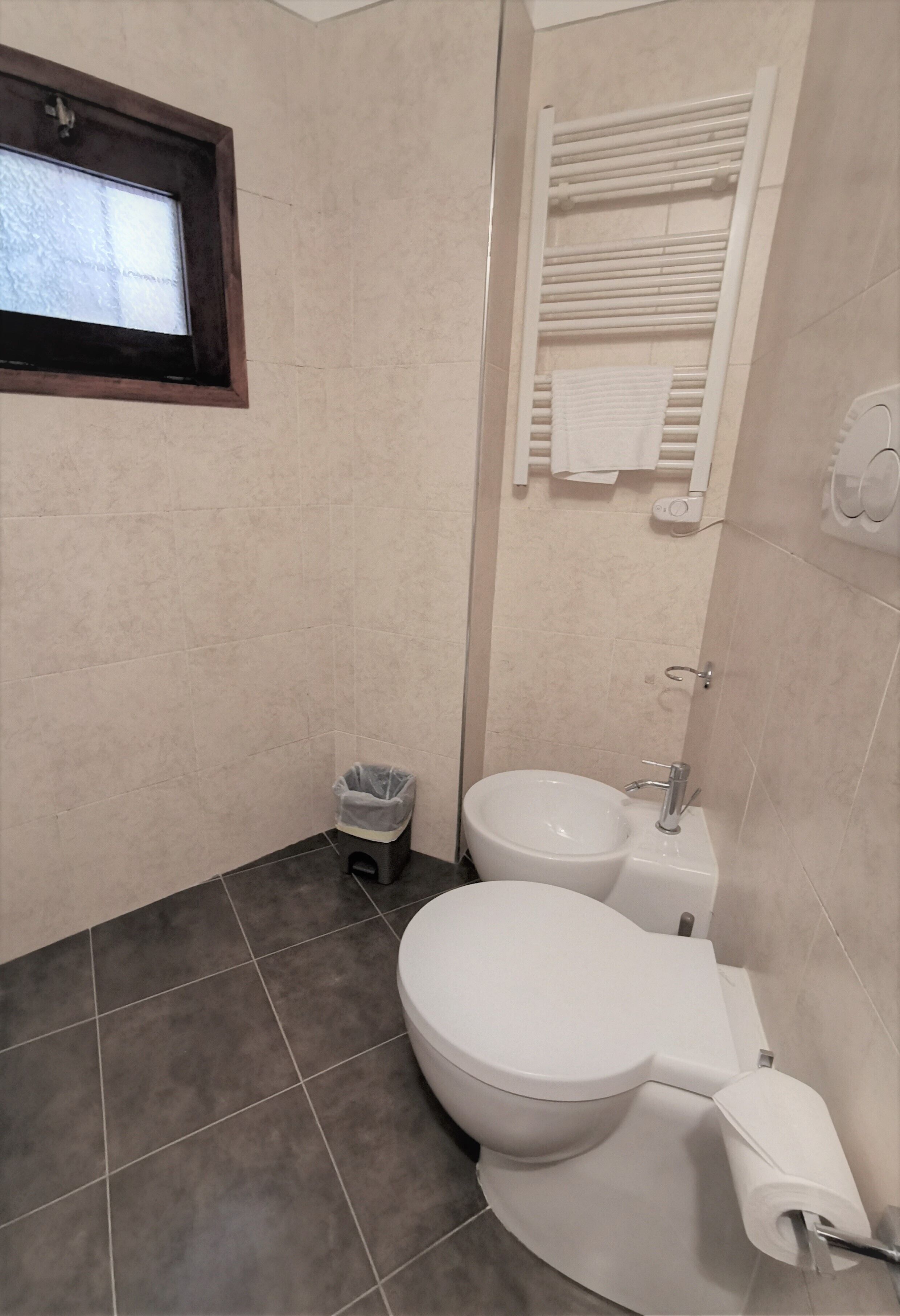 A bathroom with a toilet, bidet, and a small window.