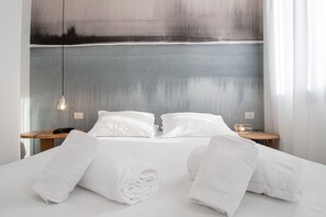A neatly made bed with white linens and towels, a bedside table with a lamp, and a painting on the wall. - Rio Hotel (Venice)