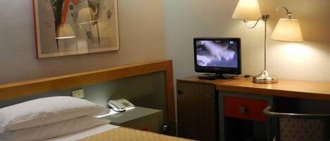 Ett hotellrum med två sängar, ett skrivbord med en dator och en telefon, en lampa och en tavla på väggen.