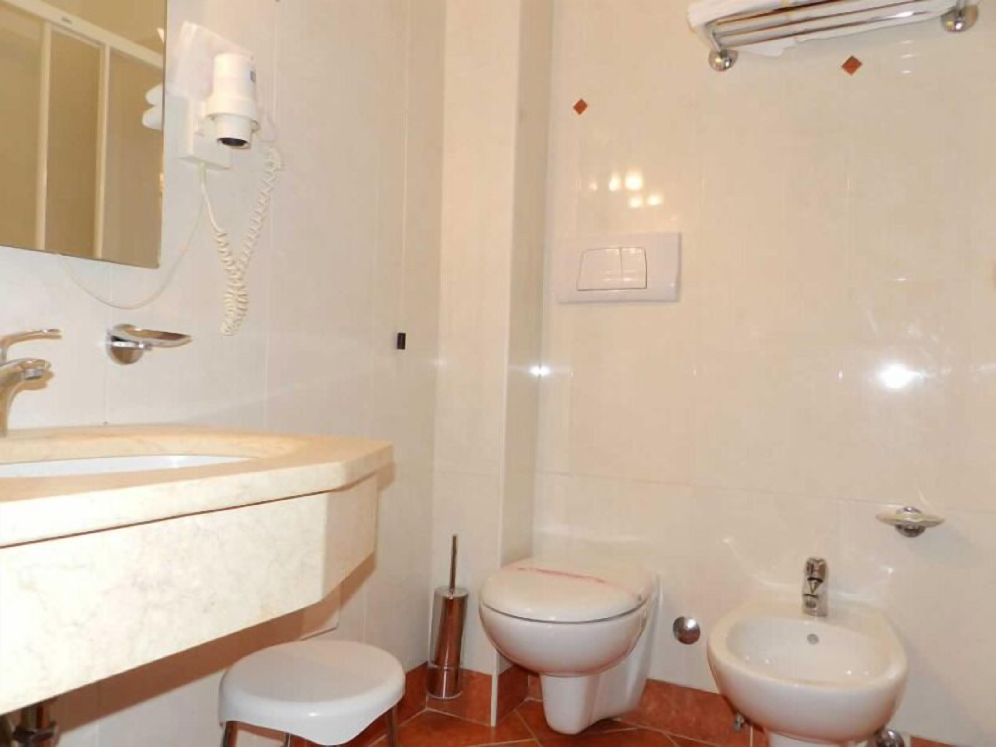 Une salle de bain équipée d’un lavabo, de toilettes, d’un bidet et d’un sèche-cheveux fixé au mur.