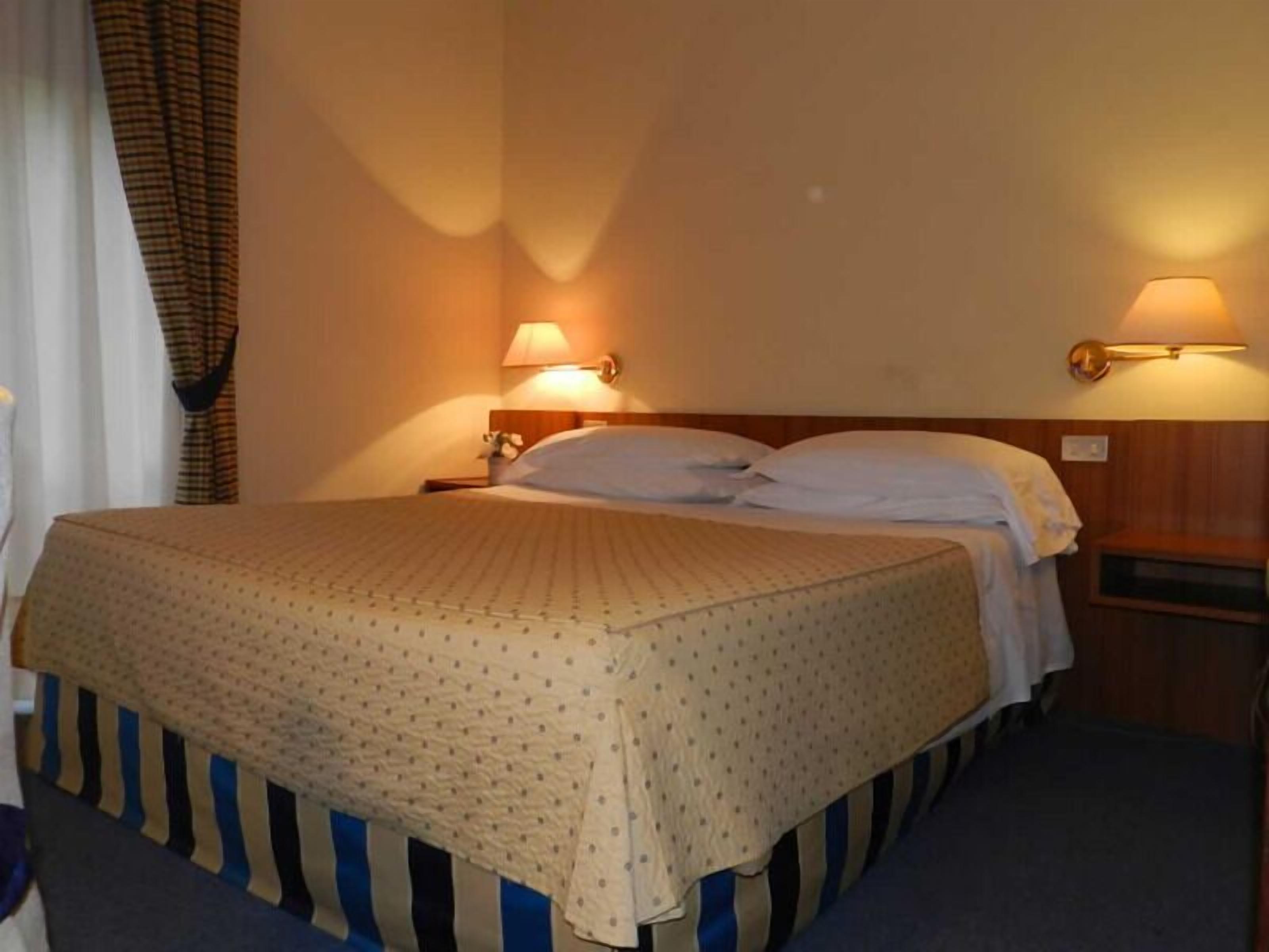 Een hotelkamer met een bed, twee bedlampen en een nachtkastje.