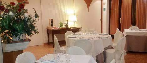 Comedor con mesas redondas dispuestas para cuatro, manteles blancos y sillas con fundas blancas.