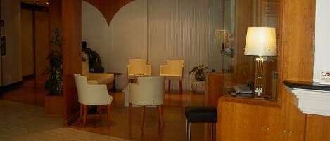 A hotel lobby with a reception desk, several chairs, a small table, and a potted plant.