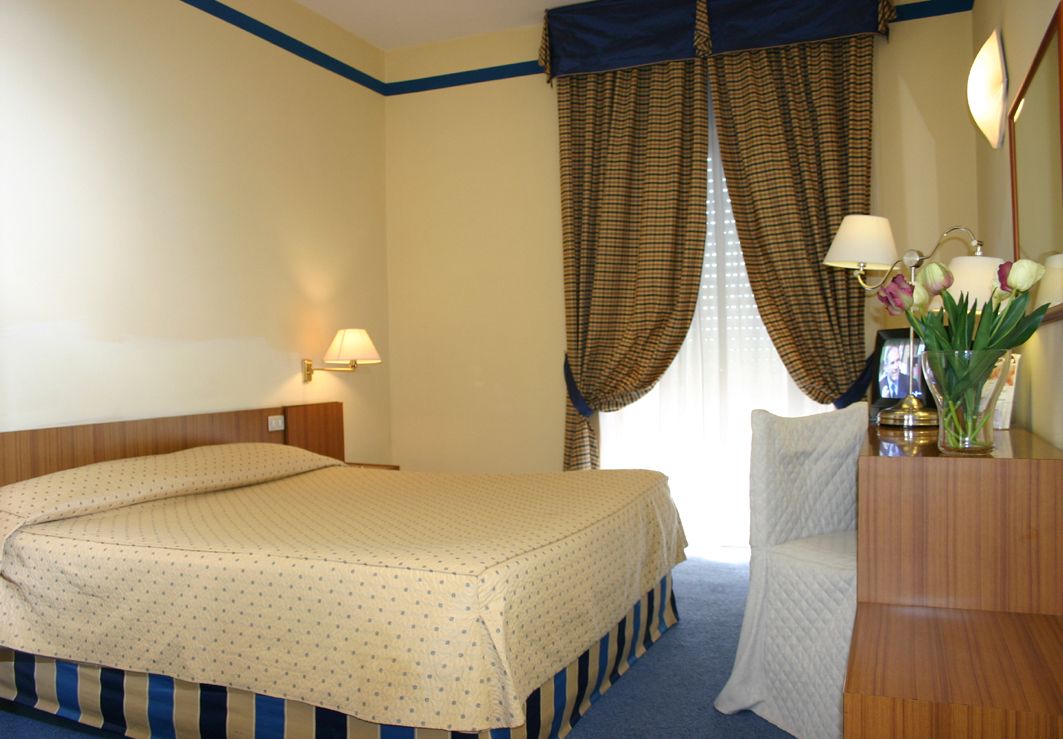 A hotel room with a bed, a desk, a lamp, and curtains.