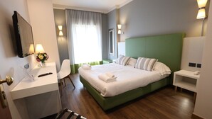 A hotel room with a green headboard, a bed with white linens, a bedside table with a lamp, a desk with a chair, and a mirror on the wall. - Umbria (Attigliano)