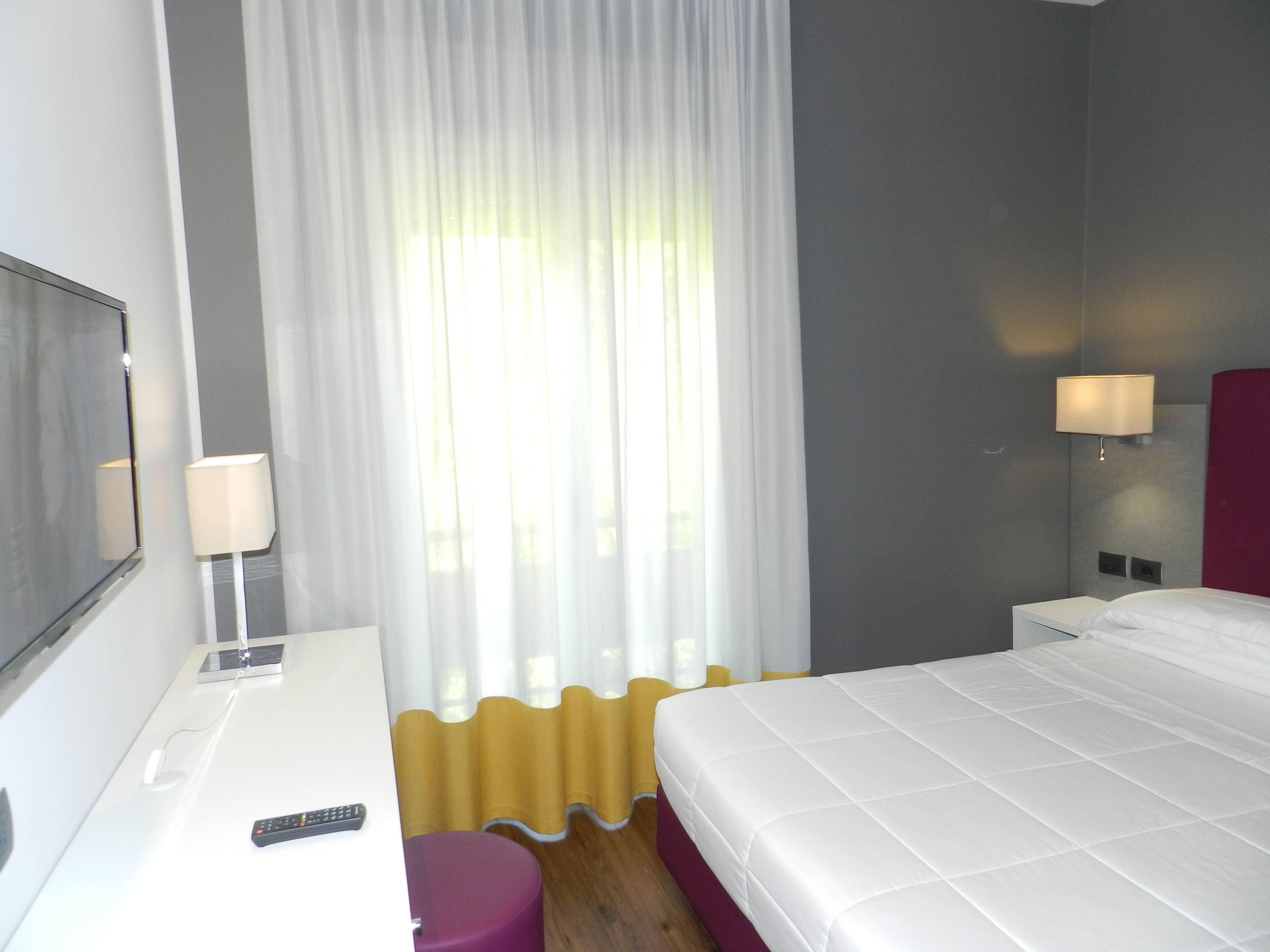 Ein Hotelzimmer mit einem Bett, einem Schreibtisch, einem Sessel, einem Fernseher und einem Fenster mit Vorhängen.