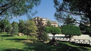 A park with a building in the background, surrounded by trees and a fence. - Umbria (Attigliano)