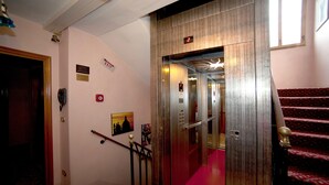 An elevator with a digital display showing the number 2, a red carpeted staircase, and a wall with a phone and a sign that says "EXIT". - Hotel Fontana (Venice)