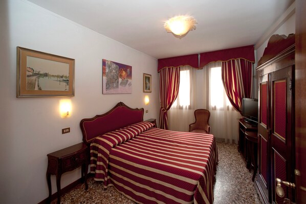 A hotel room with a large bed, a television, a desk, and a chair. - Hotel Fontana (Venice)