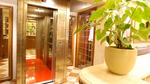 A hotel lobby with a checkered floor, a potted plant, and a glass elevator. - Hotel Fontana (Venice)