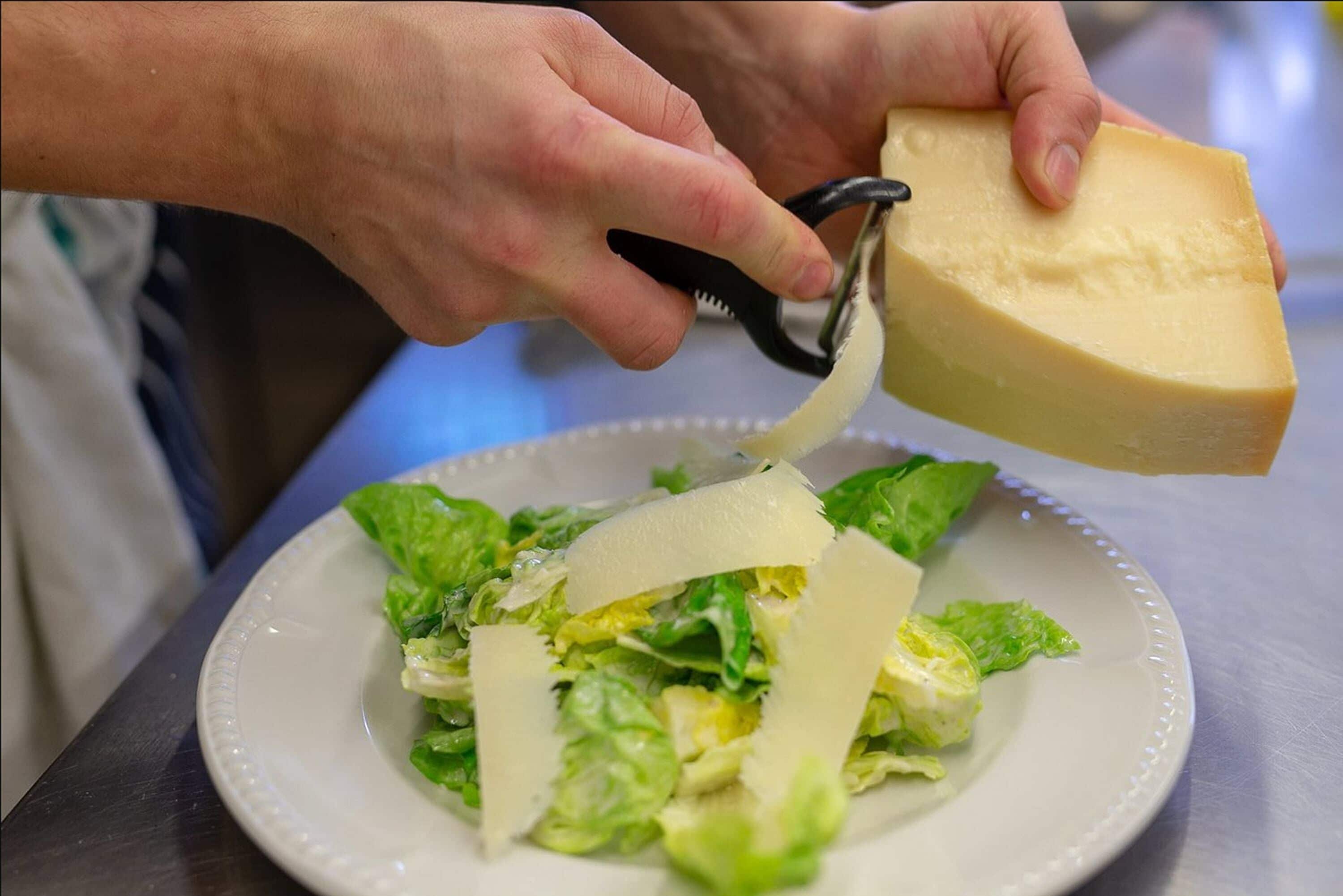 Una persona grattugia formaggio su un piatto di lattuga.