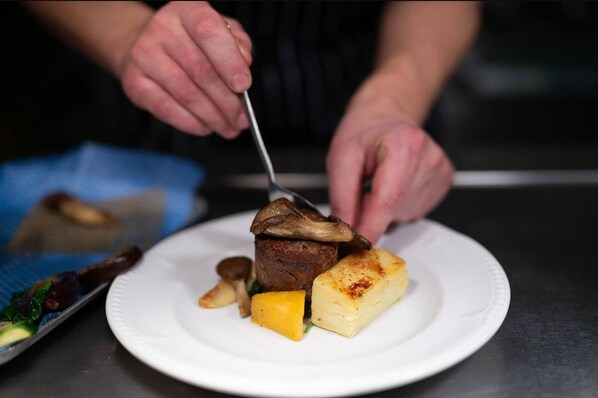 A chef slicing a steak topped with mushrooms and served with a side of mashed potatoes and vegetables.