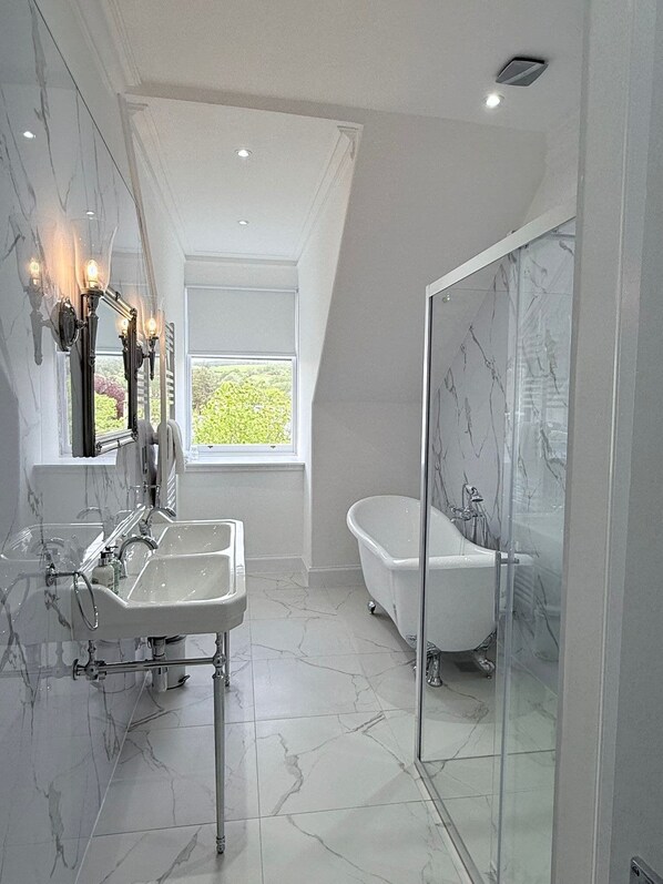 A modern bathroom with a freestanding bathtub, a glass-enclosed shower, and a large window providing natural light.
