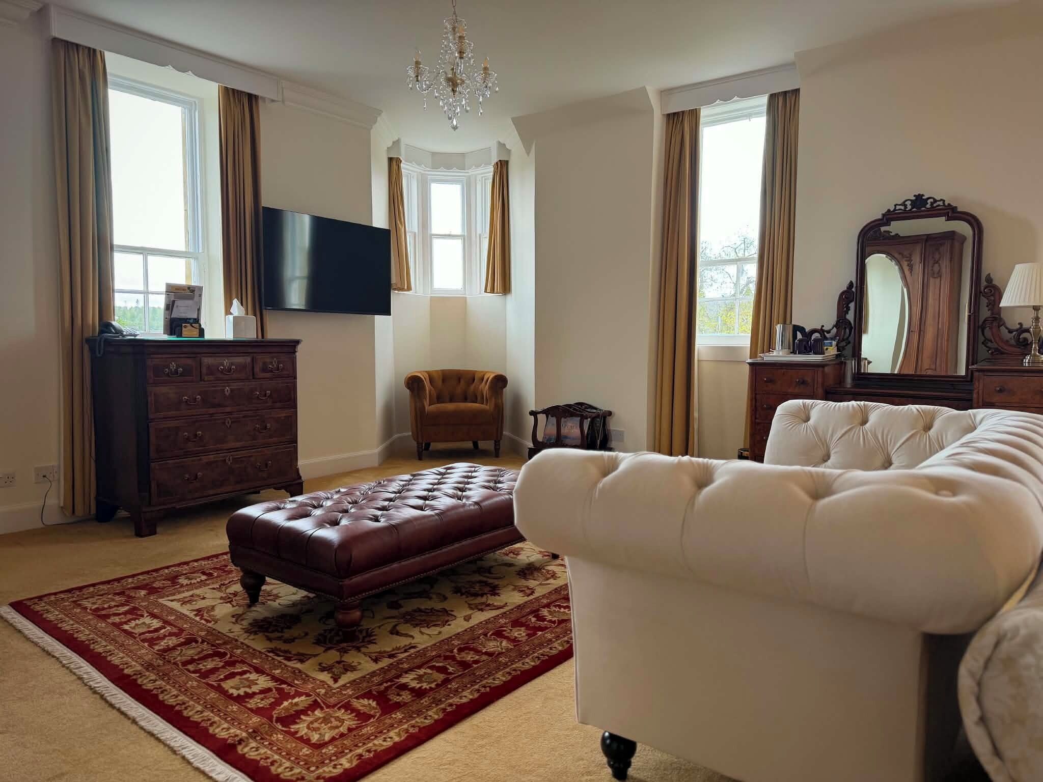 Een ruime kamer met een groot bed, een houten dressoir, een televisie en een kroonluchter.