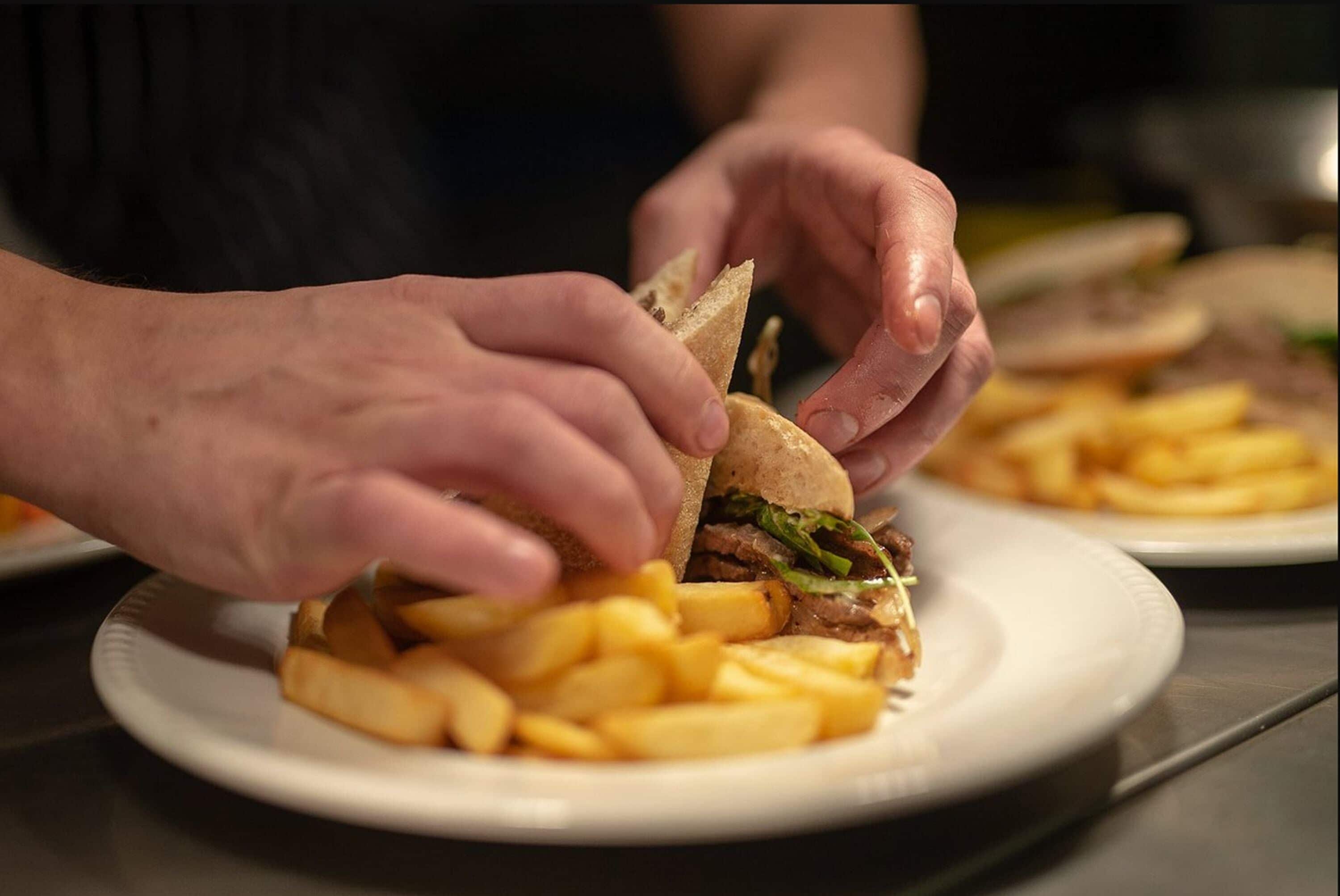 Una persona armando un sándwich con papas fritas en un plato.