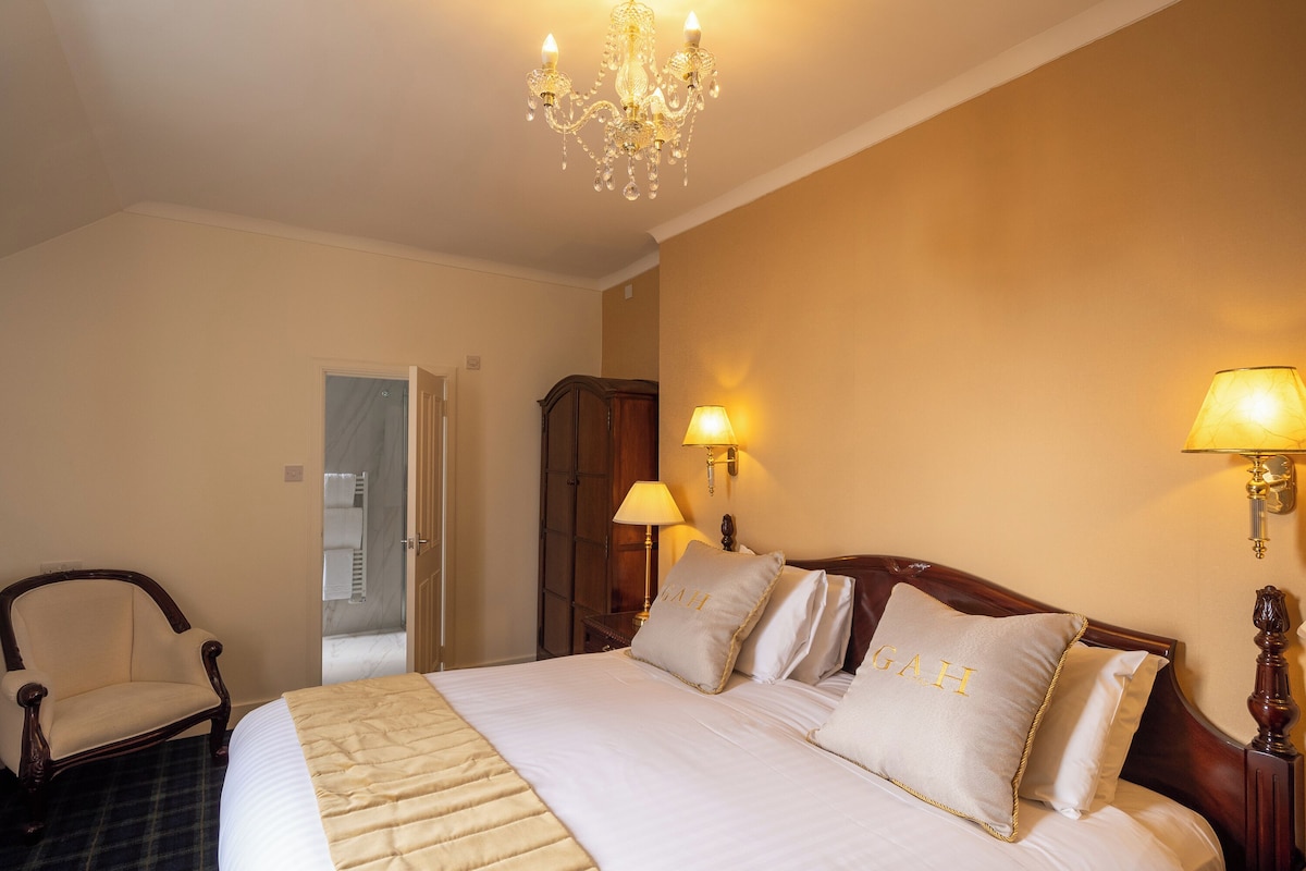 Une chambre d’hôtel avec un grand lit, deux lampes de chevet, un lustre, une chaise en bois et une armoire.