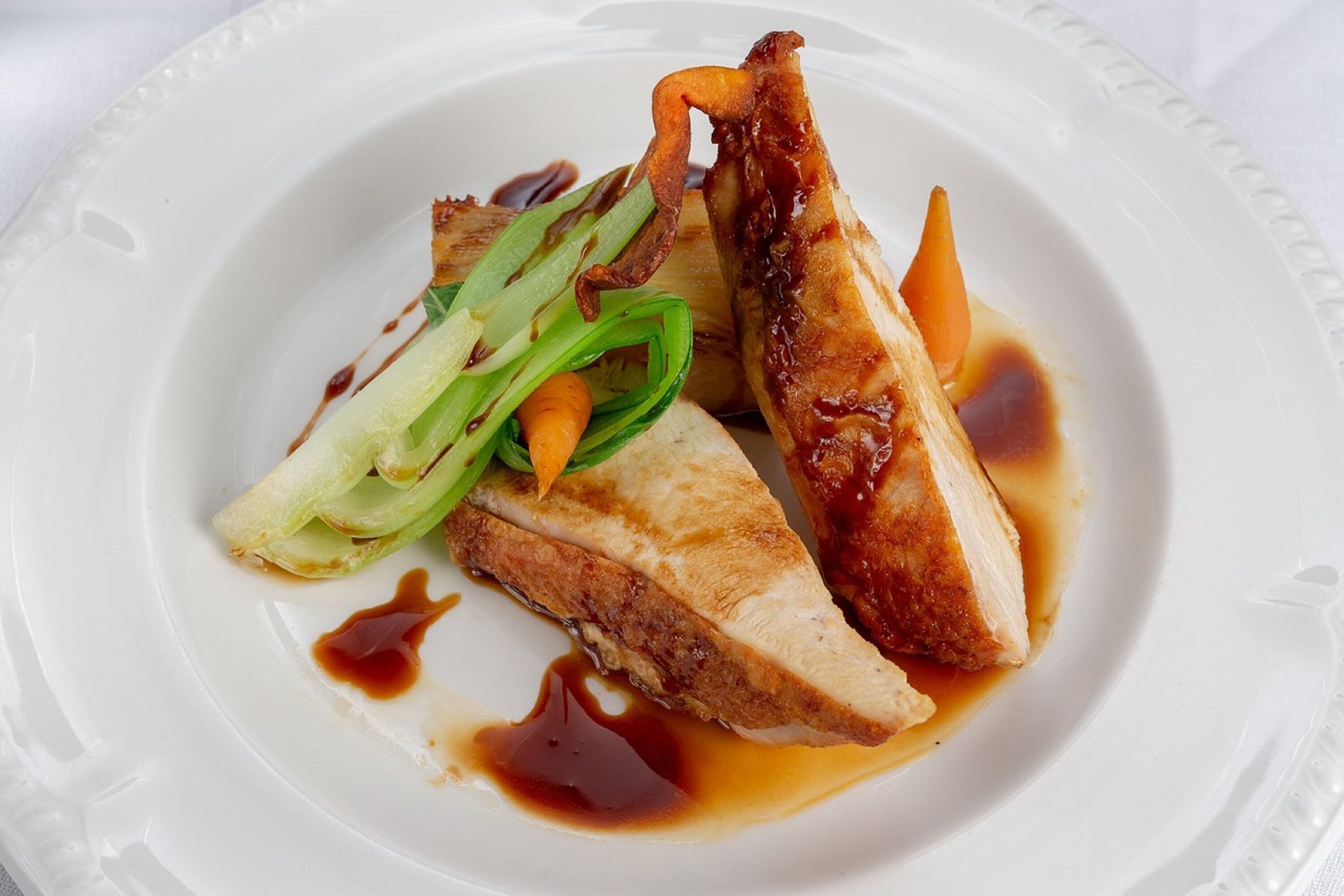 A plate with sliced meat, vegetables, and sauce.