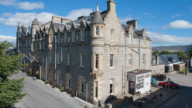 Un edificio de piedra histórica con múltiples ventanas y una torre en esquina, presumiblemente un hotel.