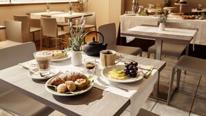 Spiseområde med borde dækket til morgenmad, inklusive croissanter, muffins og frugt.