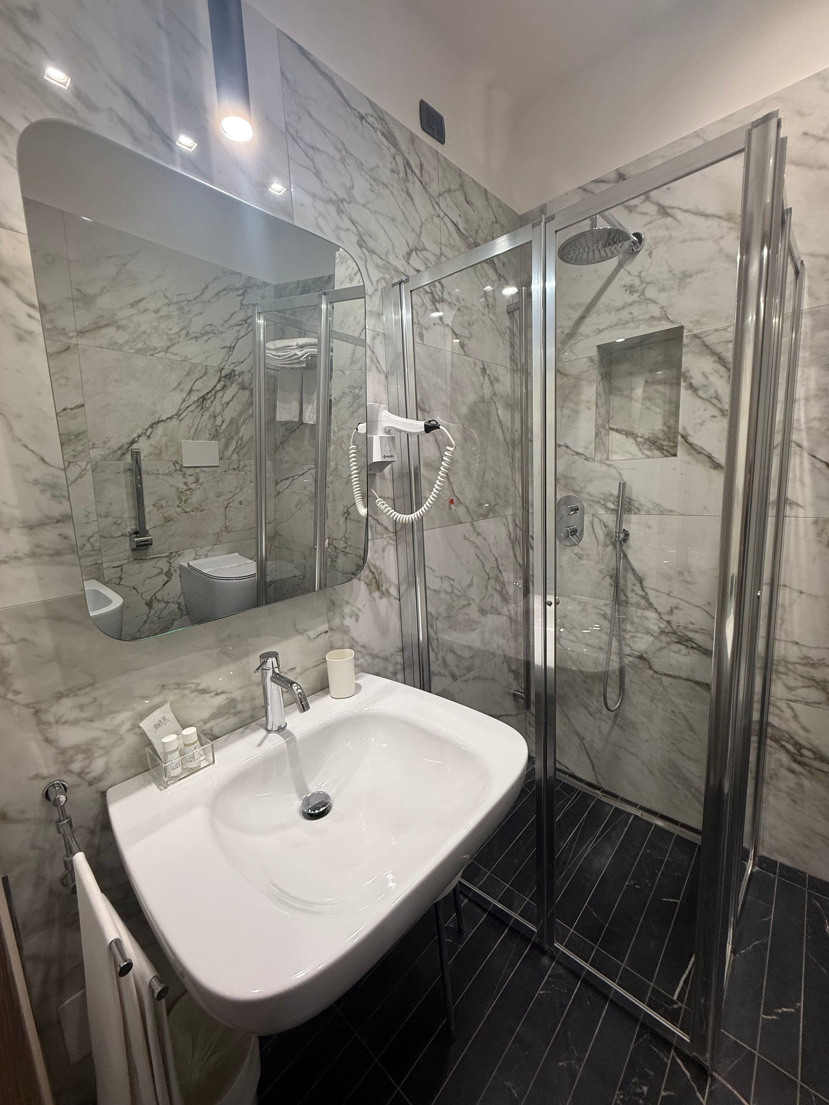 A modern bathroom with a marble vanity, a glass-enclosed shower, and a large mirror.