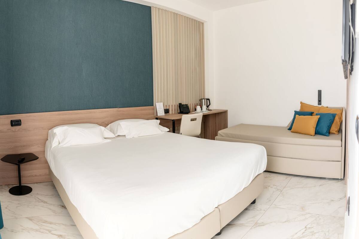 Une chambre d’hôtel moderne dotée d’un grand lit, d’un bureau avec un téléphone et une machine à café, ainsi que d’un petit canapé avec des coussins.