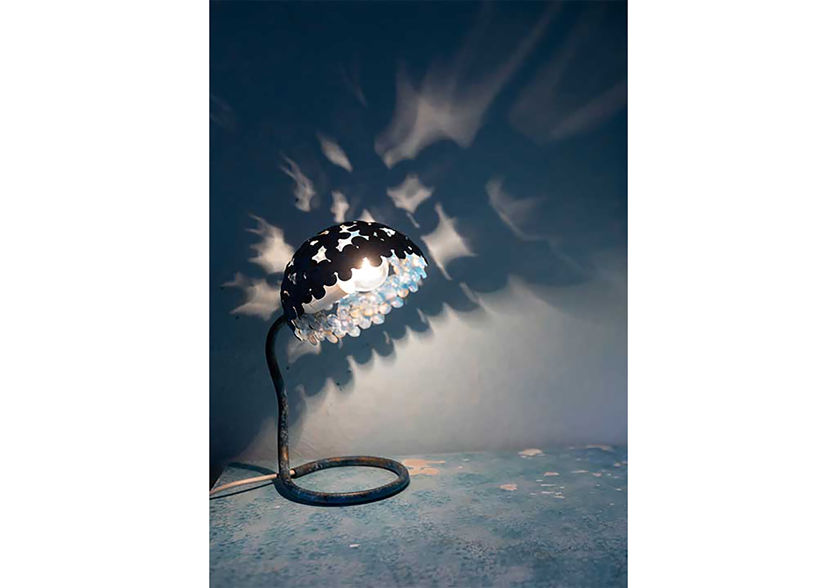 Une lampe de table avec un abat-jour orné d’un motif en étoile, un pied en spirale et une surface bleue.