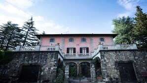 A historic building with a pink facade, two symmetrical stone gateways, and a central balcony. - Villa Rosa Panzano (Greve in Chianti)