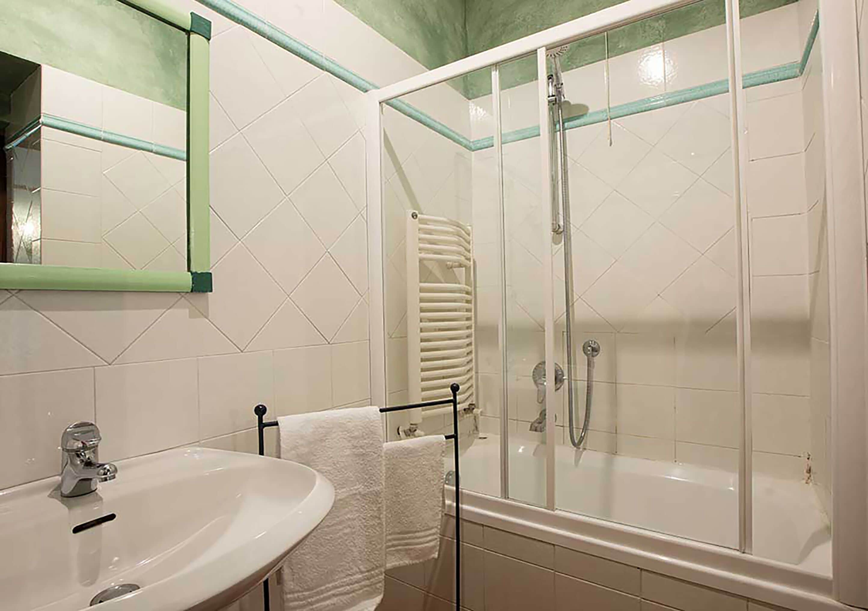 A bathroom with a sink, mirror, towel rack, and a glass-enclosed shower area.