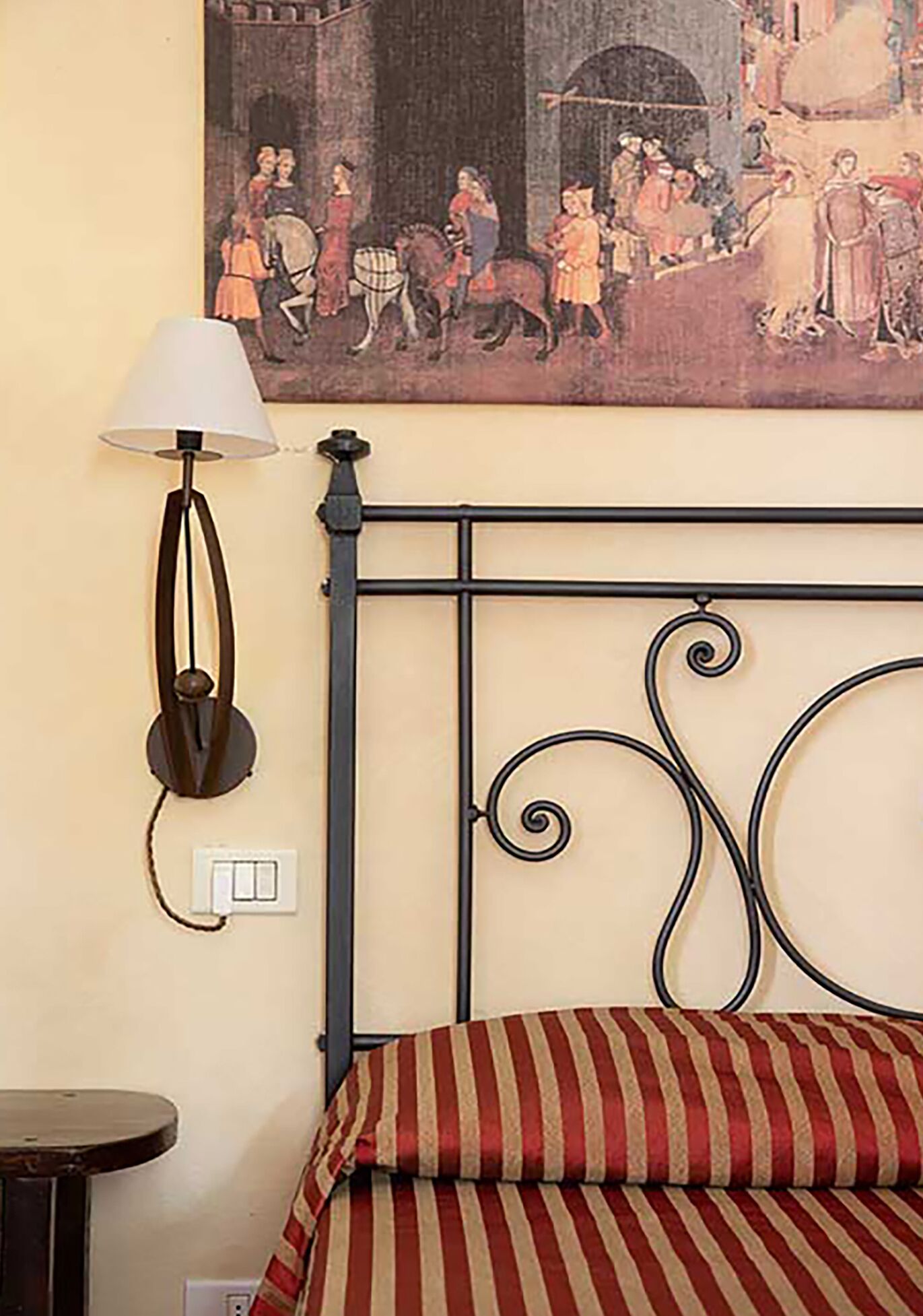 Una habitación con estructura de cama de metal, una lámpara, un cuadro y un almohadón a rayas.