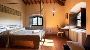 A bedroom with a bed, a desk, a chair, a window, and a radiator. - Villa Rosa Panzano (Greve in Chianti)
