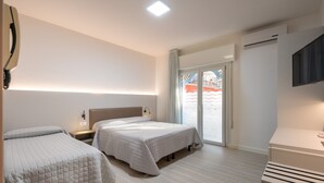 A hotel room with two beds, a flat-screen TV, an air conditioning unit, and a sliding glass door leading to a balcony. - Hotel Maxim (Caorle)