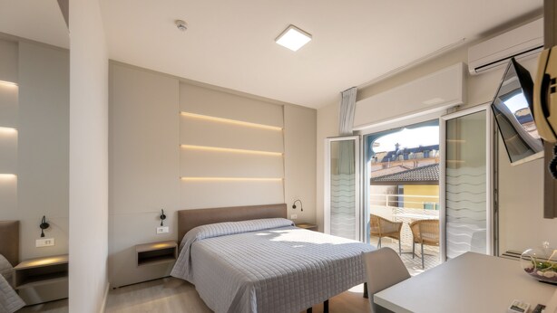 A modern hotel room with a bed, bedside table, and a view of the outside balcony. - Hotel Maxim (Caorle)