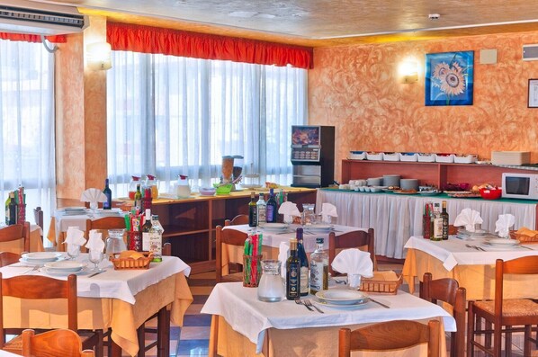 A restaurant with multiple tables set for dining, a kitchen area, and a large window with curtains. - Sole (Rosolina)
