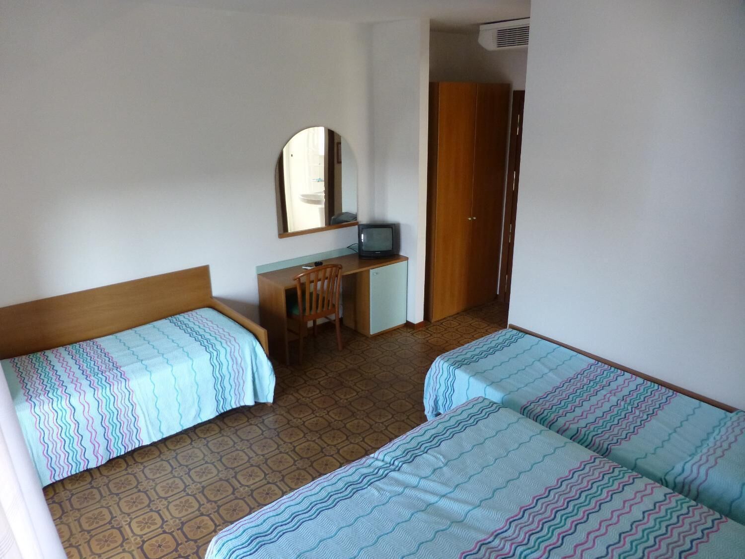 A hotel room with two beds, a desk, a chair, a television, and a wardrobe.