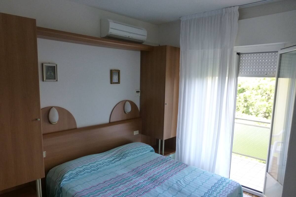 Un dormitorio con cama, armario y puerta corrediza de vidrio a un balcón.